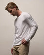 Image of a man wearing a white long sleeve tee shirt with khaki pants on a neutral background. 