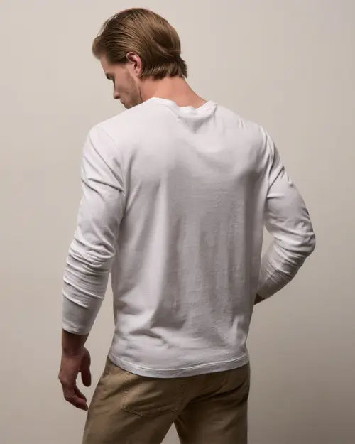 Image of the backside of a man wearing a white long sleeved tee with khaki pants on a neutral background. 