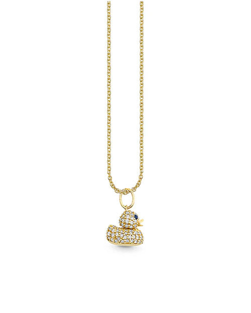 A gold necklace featuring a pendant shaped like a rubber duck, encrusted with small sparkling stones. The duck has blue stones for eyes and an orange beak. The gold chain has a simple, elegant design.
