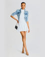 Model wearing a white dress and a blue denim jacket, holding a black shoulder bag and matching silver shoes.