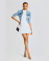 Model wearing a white dress and a blue denim jacket, holding a black shoulder bag and matching silver shoes.