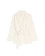 White knitted cardigan with a shawl collar, fringe detailing along the edges, long sleeves, and a matching waist tie.