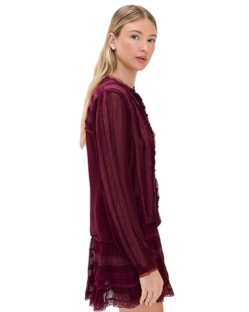 Person wearing a long-sleeved burgundy dress made of sheer fabric with lace details, intricate patterns, and layered design. 