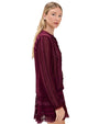Person wearing a long-sleeved burgundy dress made of sheer fabric with lace details, intricate patterns, and layered design. 