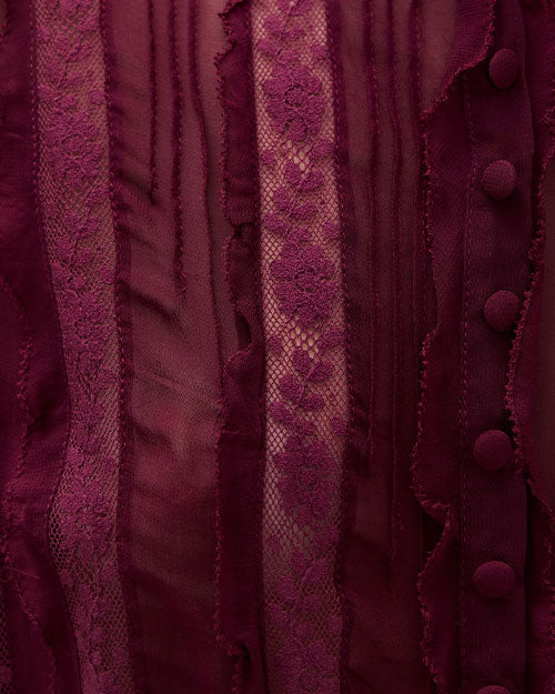 Close-up view of burgundy fabric featuring vertical stripes of lace and sheer material, with fabric-covered buttons and floral lace patterns.