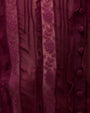 Close-up view of burgundy fabric featuring vertical stripes of lace and sheer material, with fabric-covered buttons and floral lace patterns.