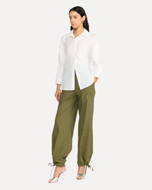 A person is wearing a white long-sleeve button down top with a pointed collar. The person is wearing green parachute pants with silver heels.