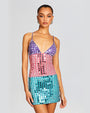 Close-up of model in a mini sequined dress with a pattern that transitions from purple at the top to turquoise at the bottom. Dress has thin straps, V-neckline and embellished with more sequence.