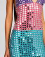 Close-up of model in a mini sequined dress with a pattern that transitions from purple at the top to turquoise at the bottom. Dress has thin straps, V-neckline and embellished with more sequence.