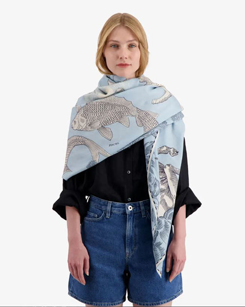 A model wearing black shirt with rolled-up sleeves and blue denim shorts. Model styled with light blue scarf with mythological creatures intertwined with ornate swirls and floral motifs.