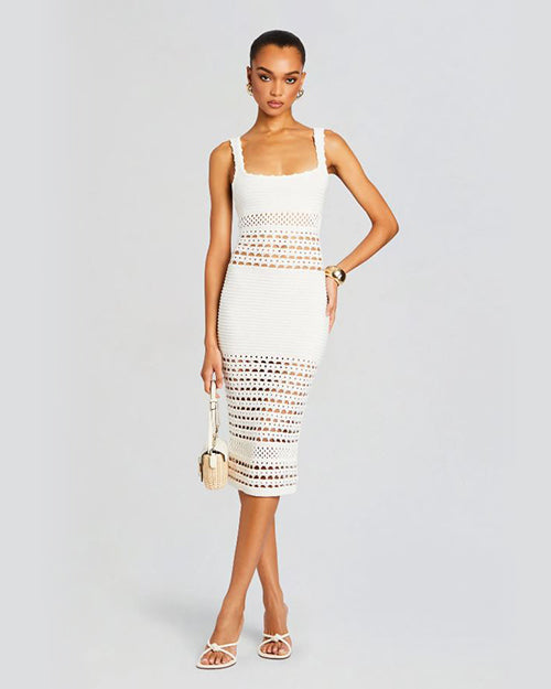 A model wearing a sleeveless knee length white crochet dress, accessorized with a bag and a white shoes. 