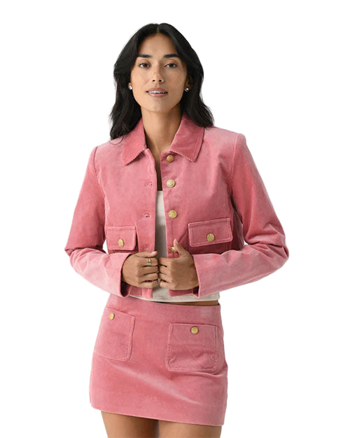 Person wearing a pink cropped jacket with long sleeves, collar, front buttons, and chest pockets with button closures, paired with a matching short skirt featuring two pockets with button closures.