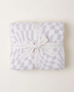 A  folded soft blanket with a white and grey pattern, meticulously tied with a ribbon that bears the brand name “BAREFOOT DREAMS.” The cozy texture and delicate packaging suggest comfort and quality.