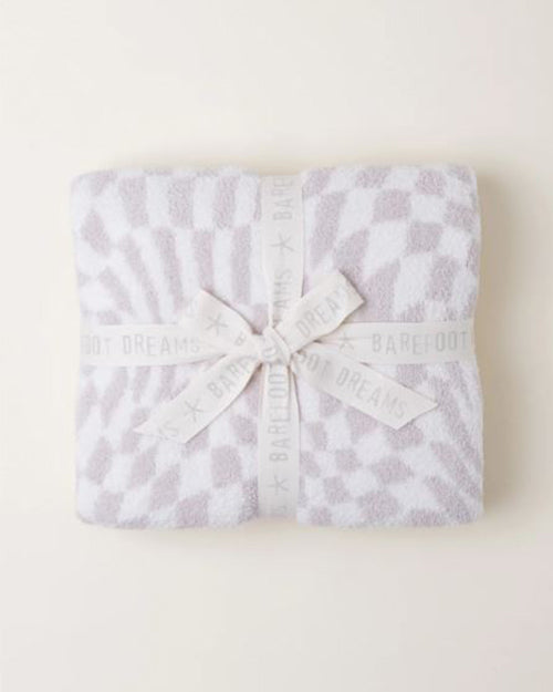 A  folded soft blanket with a white and grey pattern, meticulously tied with a ribbon that bears the brand name “BAREFOOT DREAMS.” The cozy texture and delicate packaging suggest comfort and quality.