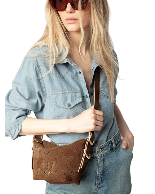 A person wearing red sunglasses, a light blue denim shirt and jeans, holding a brown leather shoulder bag with floral patterns.