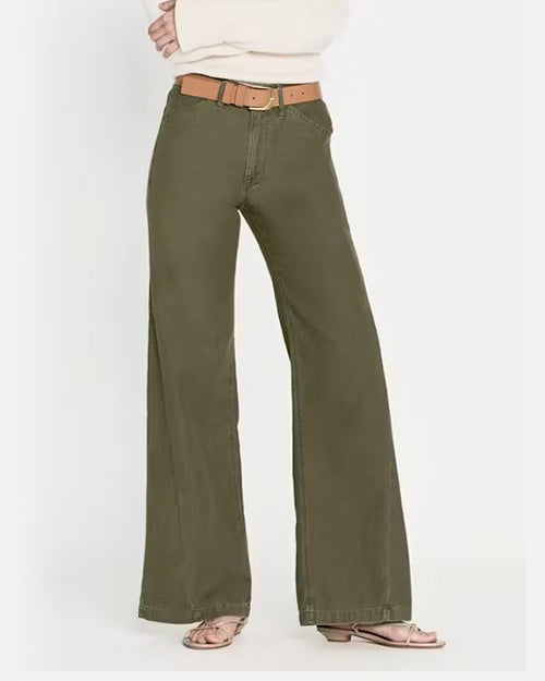 A person wearing olive green denim trousers fitted around the hips with a wide leg fit at the bottom. The trousers have a smooth texture and are paired with a light brown belt with a gold buckle. The trousers are styled with a white top, partially visible, and nude open-toe sandals. The overall look is casual yet stylish, suitable for everyday wear.