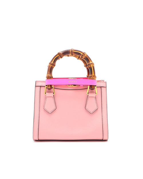 The back view of a pink designer handbag with a prominent bamboo handle and a detachable shoulder strap. The bag features gold-tone hardware, including a circular logo on the front. 