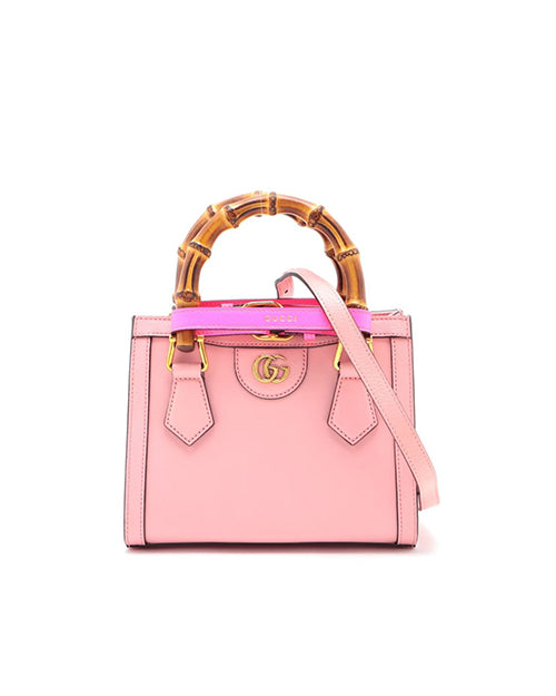 A pink designer handbag with a prominent bamboo handle and a detachable shoulder strap. The bag features gold-tone hardware, including a circular logo on the front. 