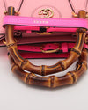 Close-up of a pink handbag with a distinctive bamboo handle. The bag features gold hardware with an interlocking double ‘G’ logo. There is a hot pink leather strap attached to one side of the handle.