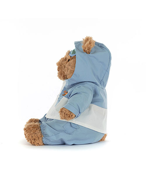 Side view of a plush teddy bear wearing a light blue and white hooded outfit, sitting upright and facing left, with soft fabric clothing covering most of its body.