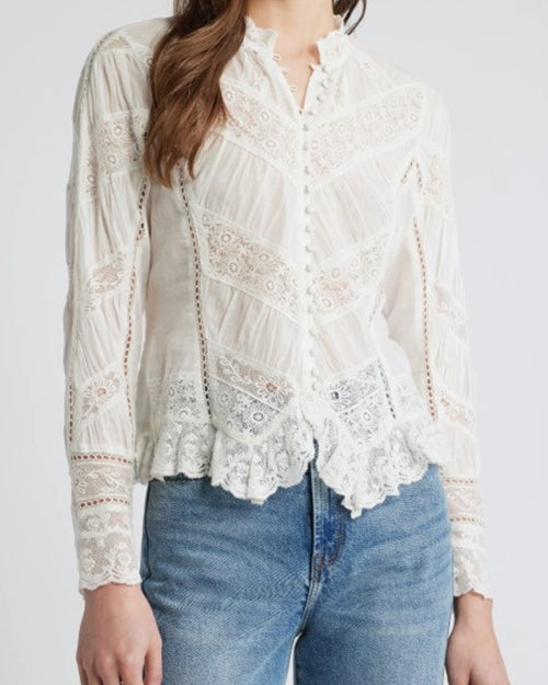A close-up torso level view of a brunette model wearing a white, long-sleeved button-down blouse with a high collar, featuring intricate lace detailing and scalloped edges at the hem and cuffs. The background is white.