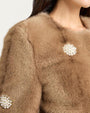 Close-up view of a light brown faux fur jacket featuring a soft plush texture and decorative pearl-like embellishments arranged in circular patterns.