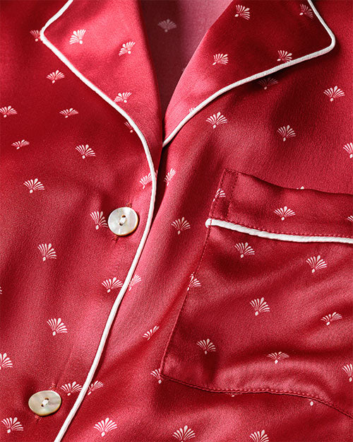 Closeup of a red pajama silk top with white art noveaux print. a pattern of small white palm-like motifs.