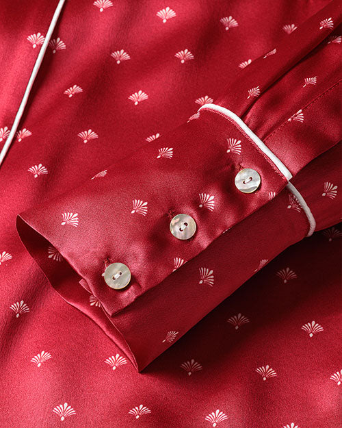 A close-up image of a silk red pajama sleeve with three buttons with a pattern of small white palm-like motifs.