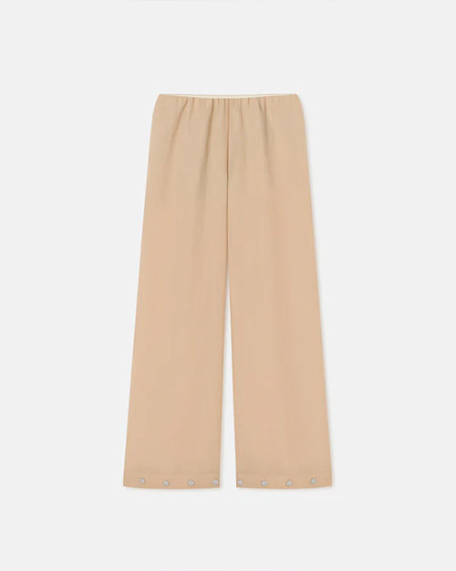Long beige flowy pants against a white background. The pants have buttons around the outside of the leg holes.