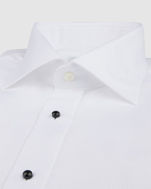 A close-up of a white dress shirt with black buttons down the front and one clear button at the top. The background is white.