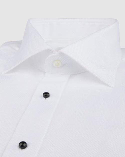 A close-up of a white dress shirt with a spread collar, black buttoned front, and long sleeves featuring rounded cuffs. 