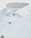 A close-up of a white dress shirt with a spread collar, grey buttoned front, and long sleeves featuring rounded cuffs. 