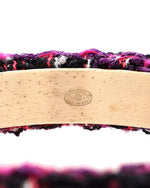 Close-up of a tweed bracelet featuring a curved wooden bar with an engraved logo.