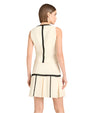 Back view of a person in a sleeveless cream skirt and top with black zigzag trim, against a white background.