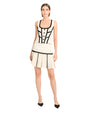 Person wearing a white two-piece set with black trim, featuring a sleeveless top and pleated skirt with black heels