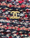 Close-up of tweed shoulder bag with a blend of red, black, white and additional color threads. The bag features a gold-tone metal logo on the front. 