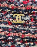 Close-up of tweed shoulder bag with a blend of red, black, white and additional color threads. The bag features a gold-tone metal logo on the front. 