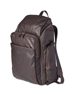 dark brown leather backpack standing against a neutral background. The backpack features a visible grain texture, a large main compartment with a zipper closure, and an additional front pocket, also with a zipper. The brand name is embossed on the lower part of the front pocket. Adjustable shoulder straps and a top handle allow for easy carrying.