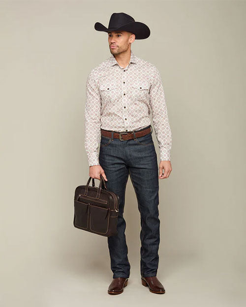 A person stands against a neutral background, wearing a cowboy hat, patterned shirt, jeans, and cowboy boots. The person is holding a dark brown leather briefcase.