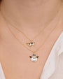 Two layered gold necklaces. The upper necklace has a cow-shaped pendant with black and white enamel, and the lower necklace features a smiley face wearing a cowboy hat with enamel detailing.