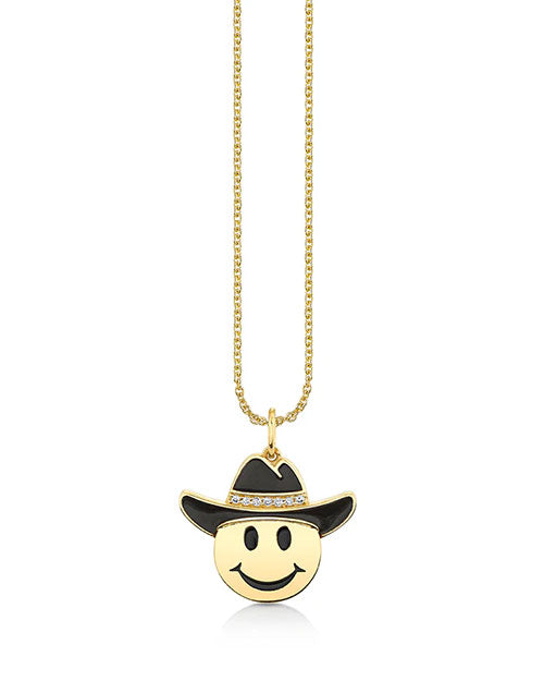Gold necklace with a pendant shaped like a yellow smiley face wearing a black cowboy hat adorned with small sparkling stones, hanging from a delicate gold chain.