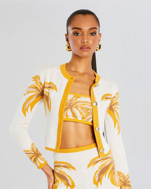 A person wearing a white and yellow cropped cardigan with a palm leaf pattern and matching high-waisted shorts and crop top.