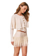 Person wearing a cream-colored long-sleeve button-up top with a scalloped hem, paired with a matching lace skirt.