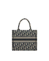 A Christian Dior designer tote bag. The bag features a repeating pattern of the brand’s initials, ‘CD,’ in a gray and blue ecru color scheme. A blue ecru stripe runs across the middle.