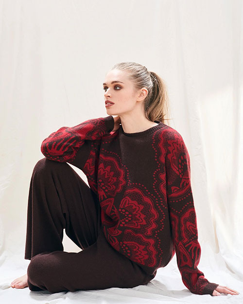 Person sitting cross-legged on the floor, wearing a dark brown sweater with red floral patterns and matching dark brown pants. 