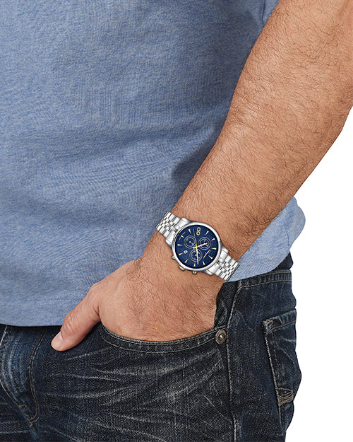 Close up of a person wearing a silver watch with a blue face on a plain background.