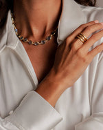 A person wearing a white shirt, a necklace with round stones, and three gold rings on the right hand.