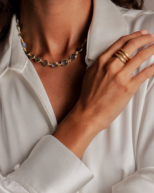 A person wearing a white shirt, a necklace with round stones, and three gold rings on the right hand.