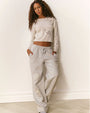 Person standing against a plain wall wearing a light-colored cropped sweater and matching light gray sweatpants, both featuring bow shaped cut-out designs.
