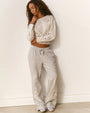 Person standing against a wall wearing a light-colored long-sleeve crop top and light gray sweatpants, both featuring embroidered bow shaped designs.
